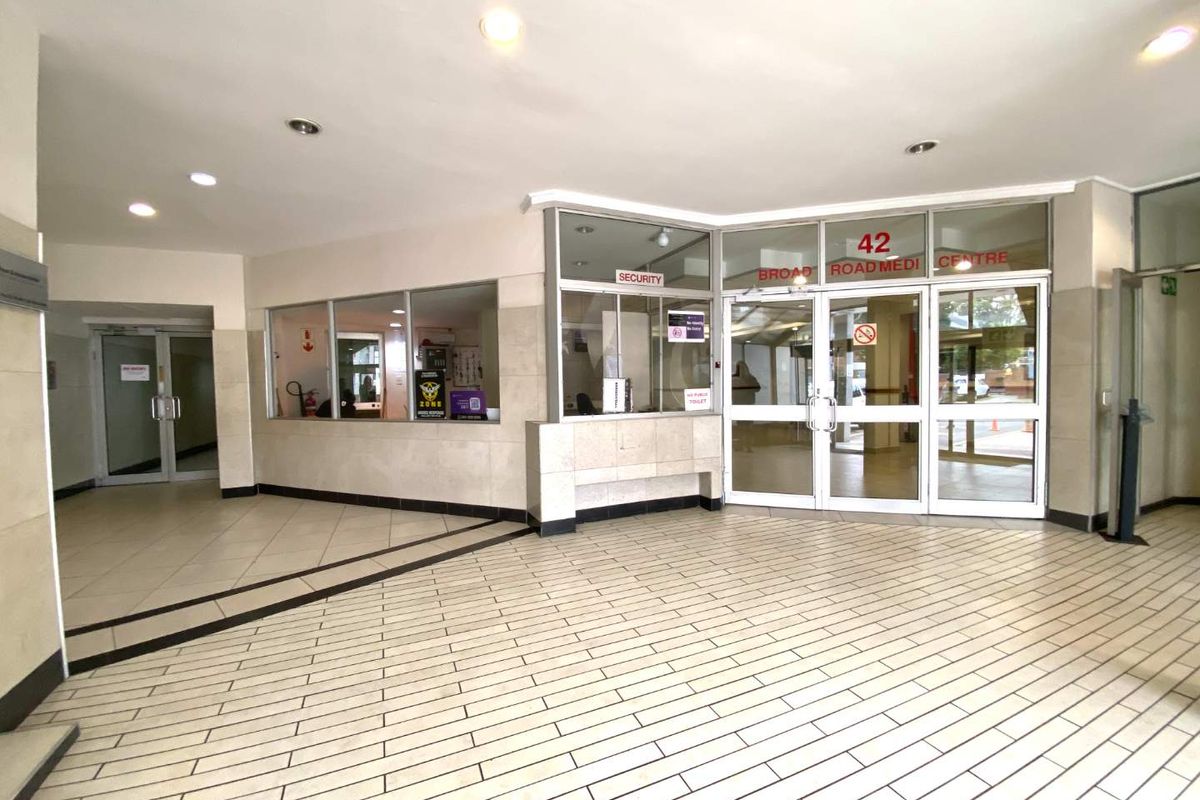 A bright and spacious building entrance lobby featuring tiled flooring, a dedicated security office, and glass-paneled double entrance doors.