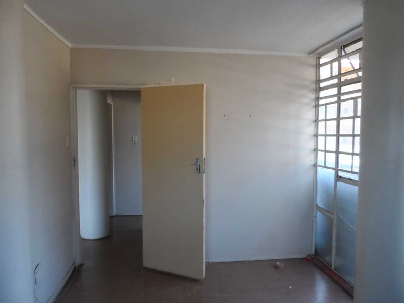 An empty bedroom featuring tiled flooring, a standard internal door, and a window fitted with security bars.