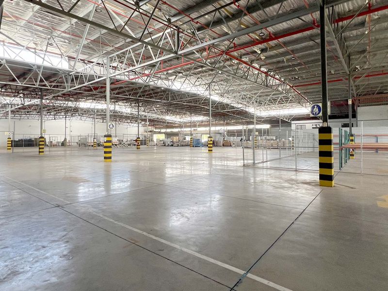 Expansive industrial warehouse space featuring high ceilings with exposed steel trusses, concrete flooring, and integrated fire sprinkler systems.