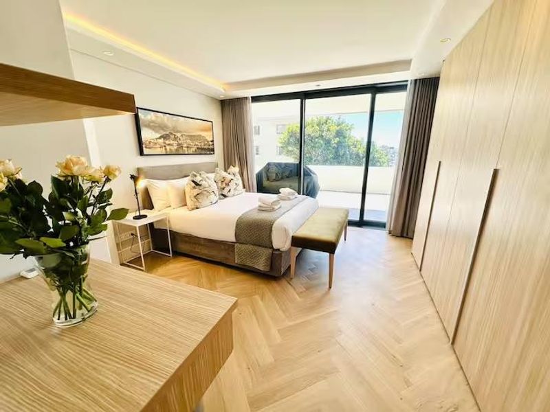Modern bedroom featuring high-quality herringbone timber flooring, extensive built-in cabinetry, and large sliding doors providing access to a private balcony.