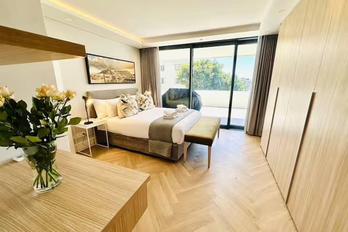 Modern bedroom featuring high-quality herringbone timber flooring, extensive built-in cabinetry, and large sliding doors providing access to a private balcony.