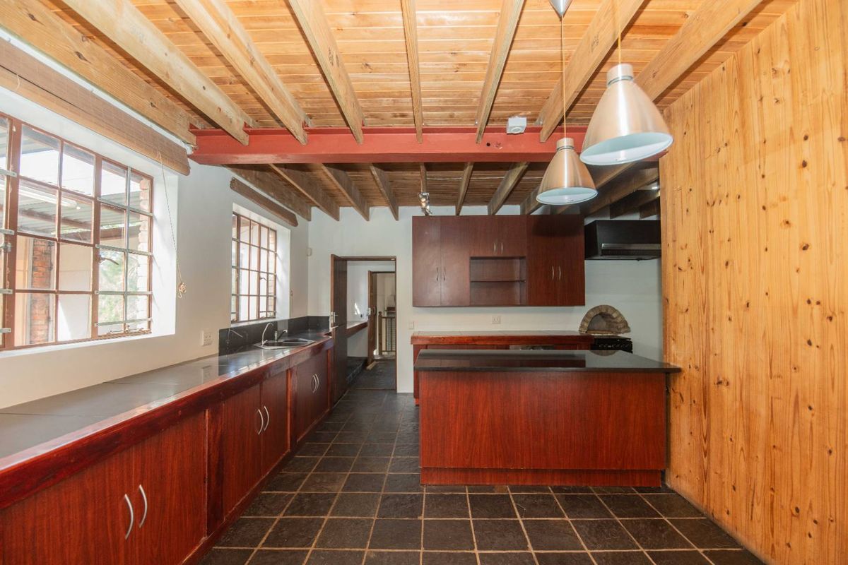 Spacious kitchen featuring timber ceilings, exposed steel beams, dark stone countertops, built-in cabinetry, and a unique integrated pizza oven.