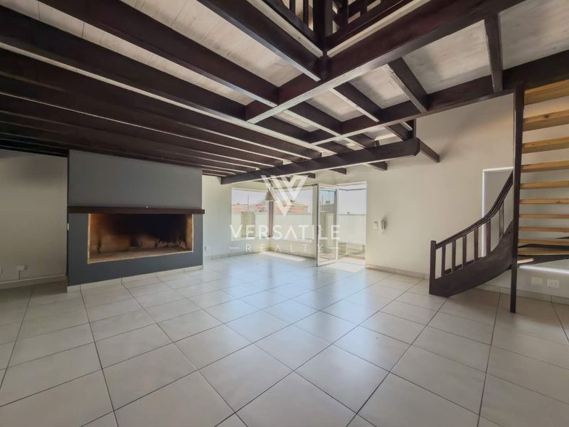 Spacious living area featuring exposed timber ceiling beams, a built-in fireplace, tiled flooring, and a timber staircase leading to an upper level.