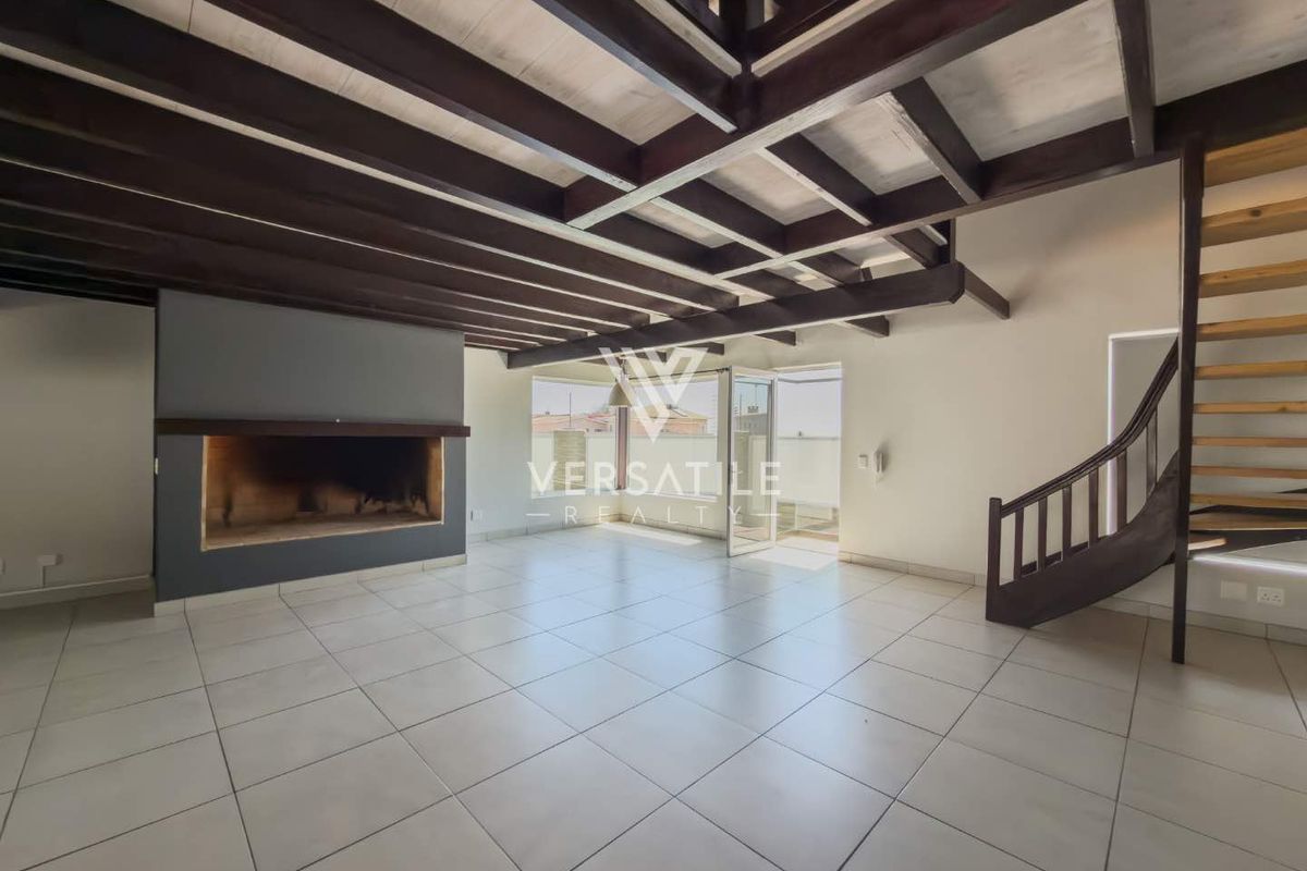 Spacious living area featuring exposed timber ceiling beams, a built-in fireplace, tiled flooring, and a timber staircase leading to an upper level.