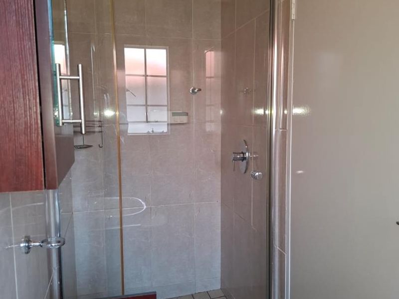 A functional bathroom featuring a glass-enclosed shower with tiled walls and a modern vanity basin.