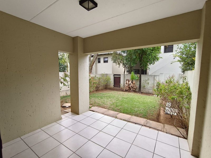 A covered patio area featuring tiled flooring, overlooking a private garden space enclosed by boundary walls.