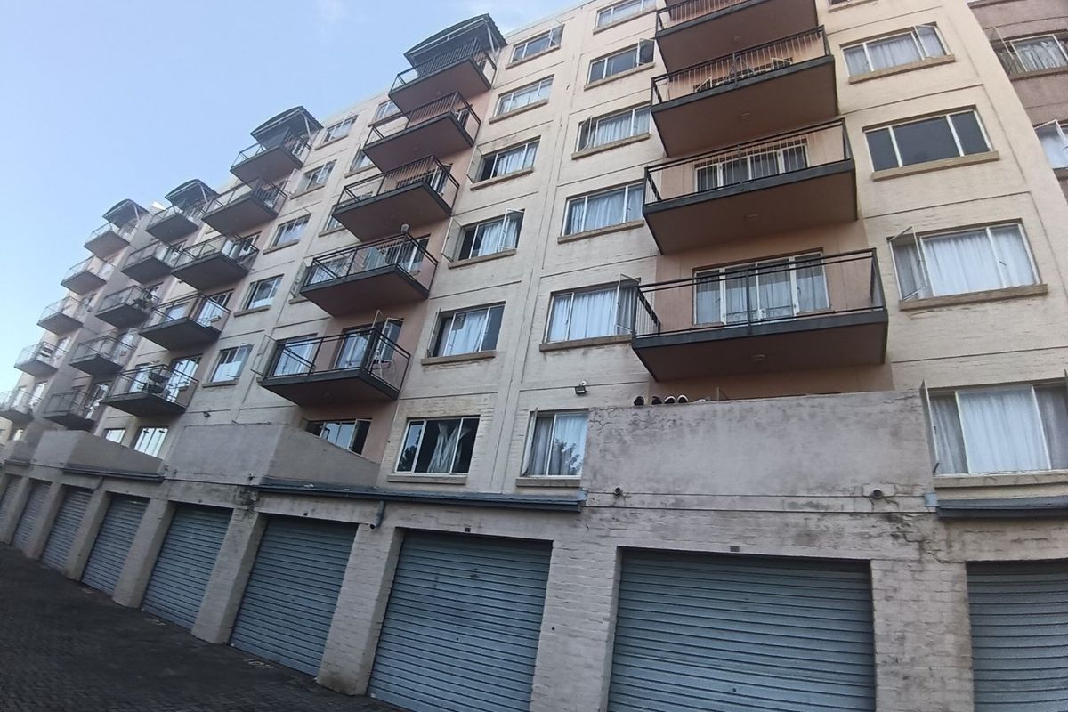 Rear elevation of a multi-story apartment building featuring multiple balconies and a row of ground-level roller shutter garage doors.