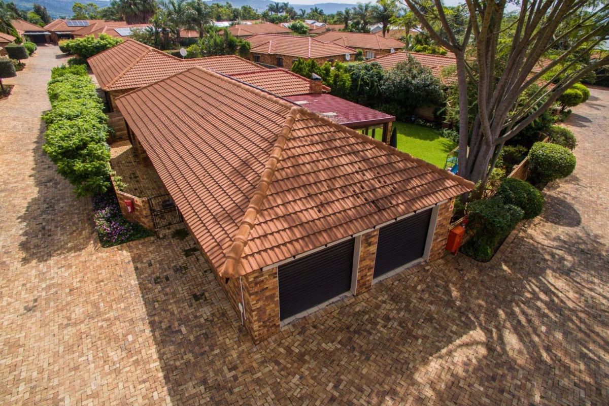 Aerial view of a townhouse complex featuring a double garage with tiled roofing and paved driveway access.