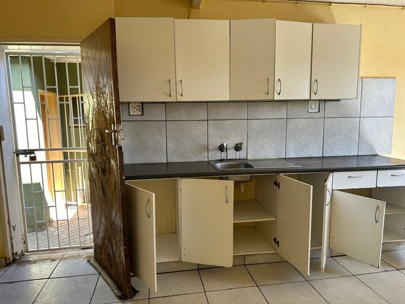 A dated kitchen area featuring basic built-in cabinetry, a stainless steel sink, and tiled backsplash, requiring renovation to modernize the space.