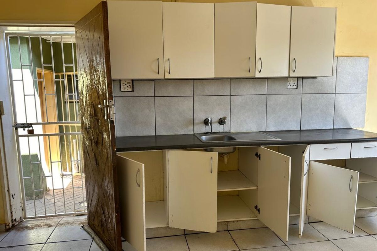 A dated kitchen area featuring basic built-in cabinetry, a stainless steel sink, and tiled backsplash, requiring renovation to modernize the space.