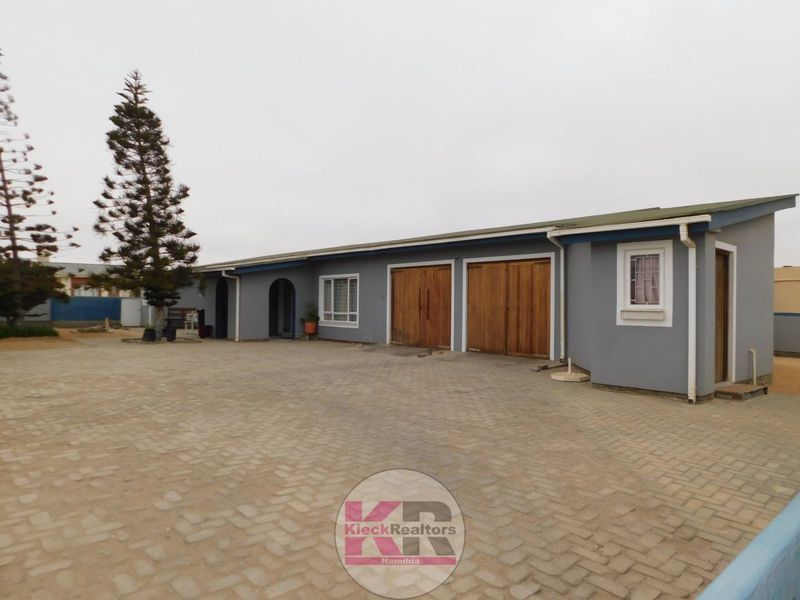 Front exterior view of a single-story house featuring a large paved driveway and double timber garage doors.