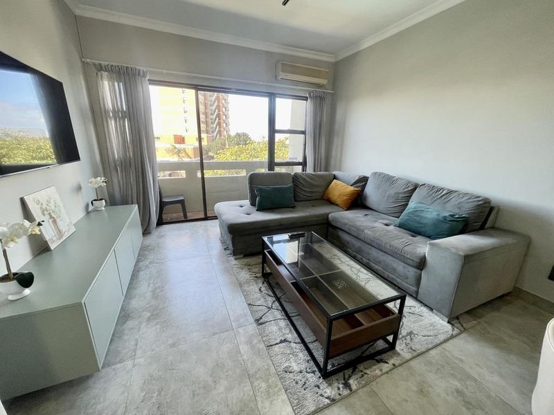 A well-maintained living room featuring large format floor tiles, a split-system air conditioner, and a sliding glass door providing access to the balcony.