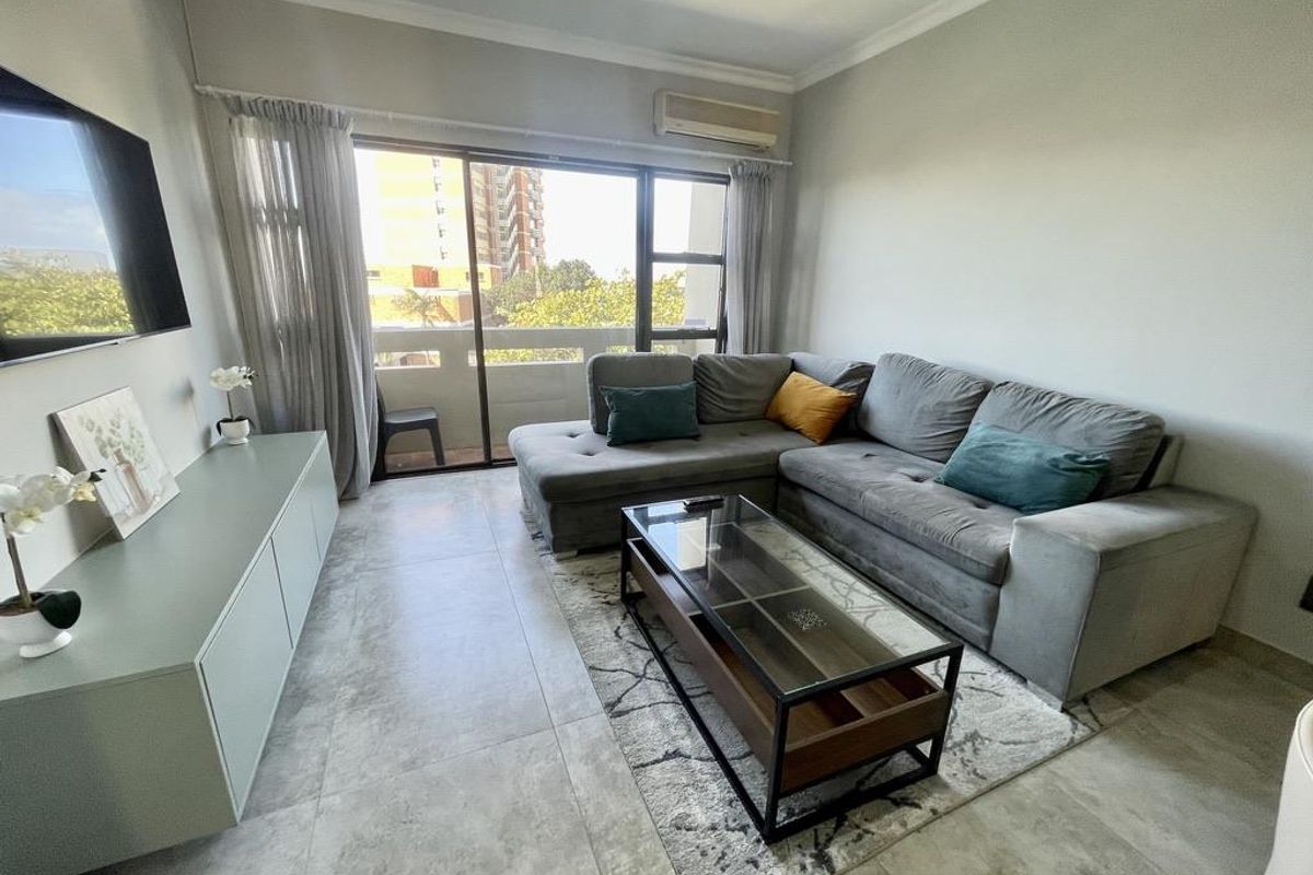 A well-maintained living room featuring large format floor tiles, a split-system air conditioner, and a sliding glass door providing access to the balcony.