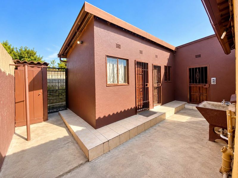 A well-maintained rear exterior area featuring tiled patio space, secure metal gates, and a functional external wash basin.
