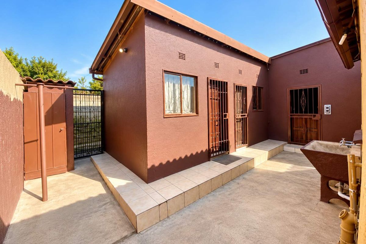 A well-maintained rear exterior area featuring tiled patio space, secure metal gates, and a functional external wash basin.