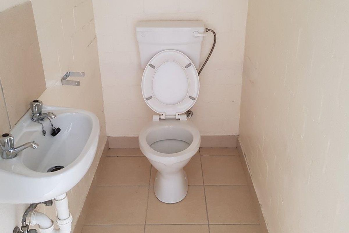 A compact industrial restroom featuring a standard ceramic toilet and a wall-mounted basin with exposed plumbing fixtures.
