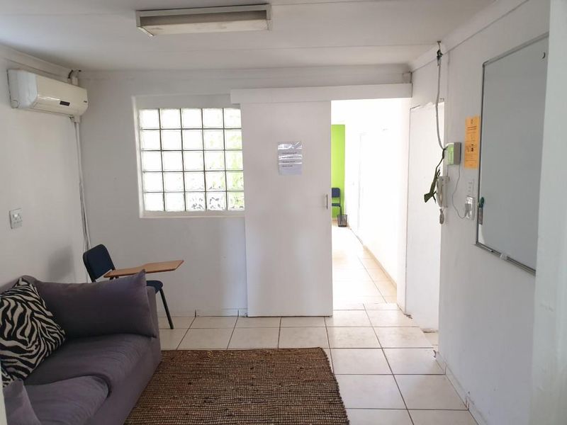 Functional office space featuring ceramic floor tiles, a glass block window, wall-mounted air conditioning, and a sliding door leading to an adjacent area.