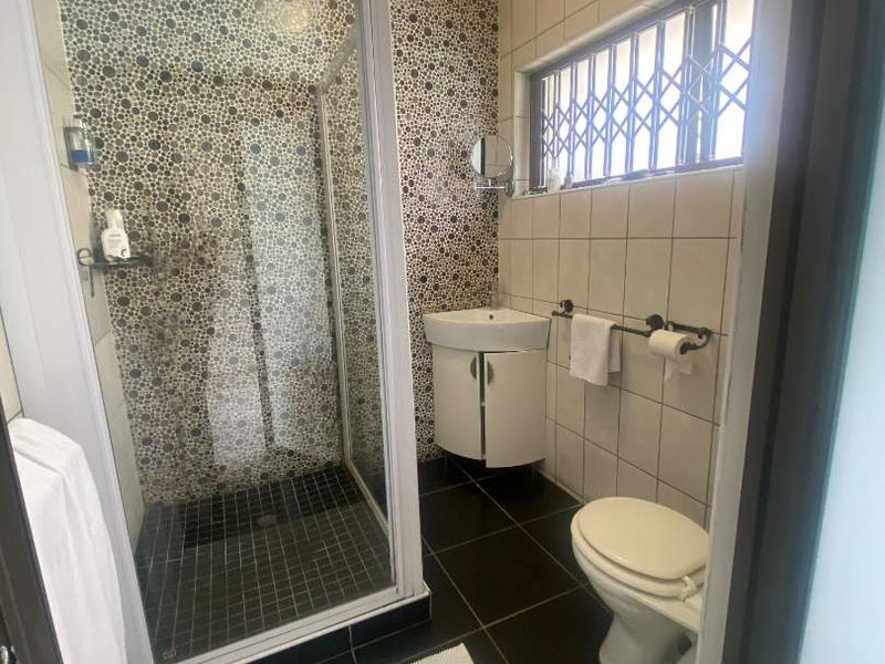 A functional bathroom featuring a shower enclosure, pedestal vanity, toilet, and decorative tiled wall accents.