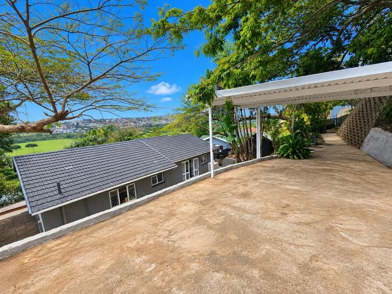 Rear exterior view featuring a concrete patio area with a covered pergola, overlooking the property roofline and surrounding landscape.