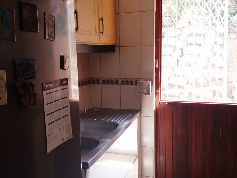 A functional scullery area featuring built-in cabinetry, a stainless steel sink, tiled splashbacks, and direct access to the exterior via a timber door.