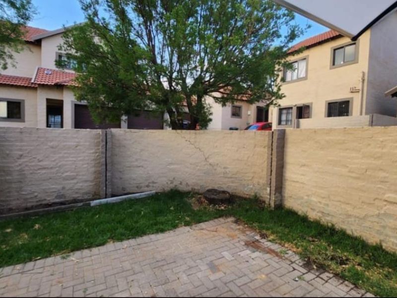 A rear garden area featuring a paved patio, small lawn, and a boundary wall showing signs of wear and cracking.