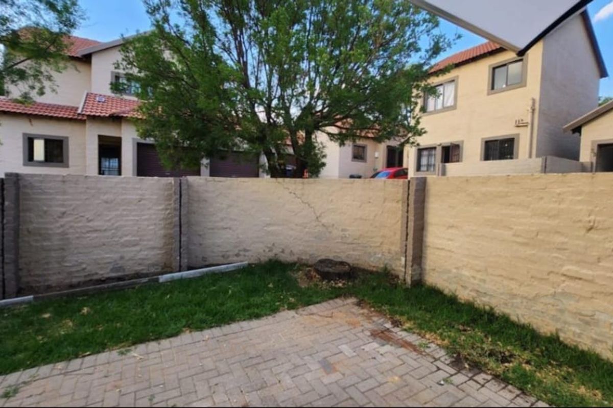 A rear garden area featuring a paved patio, small lawn, and a boundary wall showing signs of wear and cracking.