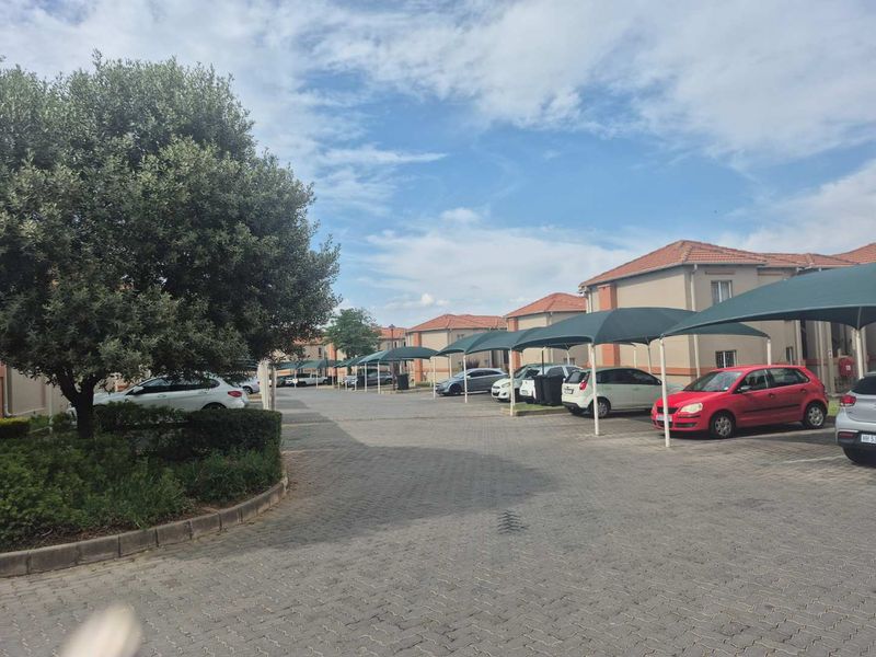 Exterior view of a townhouse complex featuring paved driveways, covered parking bays, and well-maintained communal garden areas.