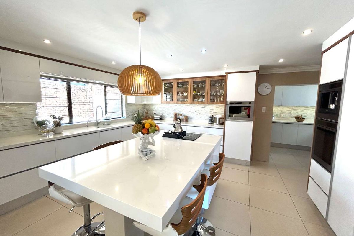 Modern kitchen featuring a large central island with quartz countertops, integrated appliances, sleek cabinetry, and a secondary scullery area visible in the background.