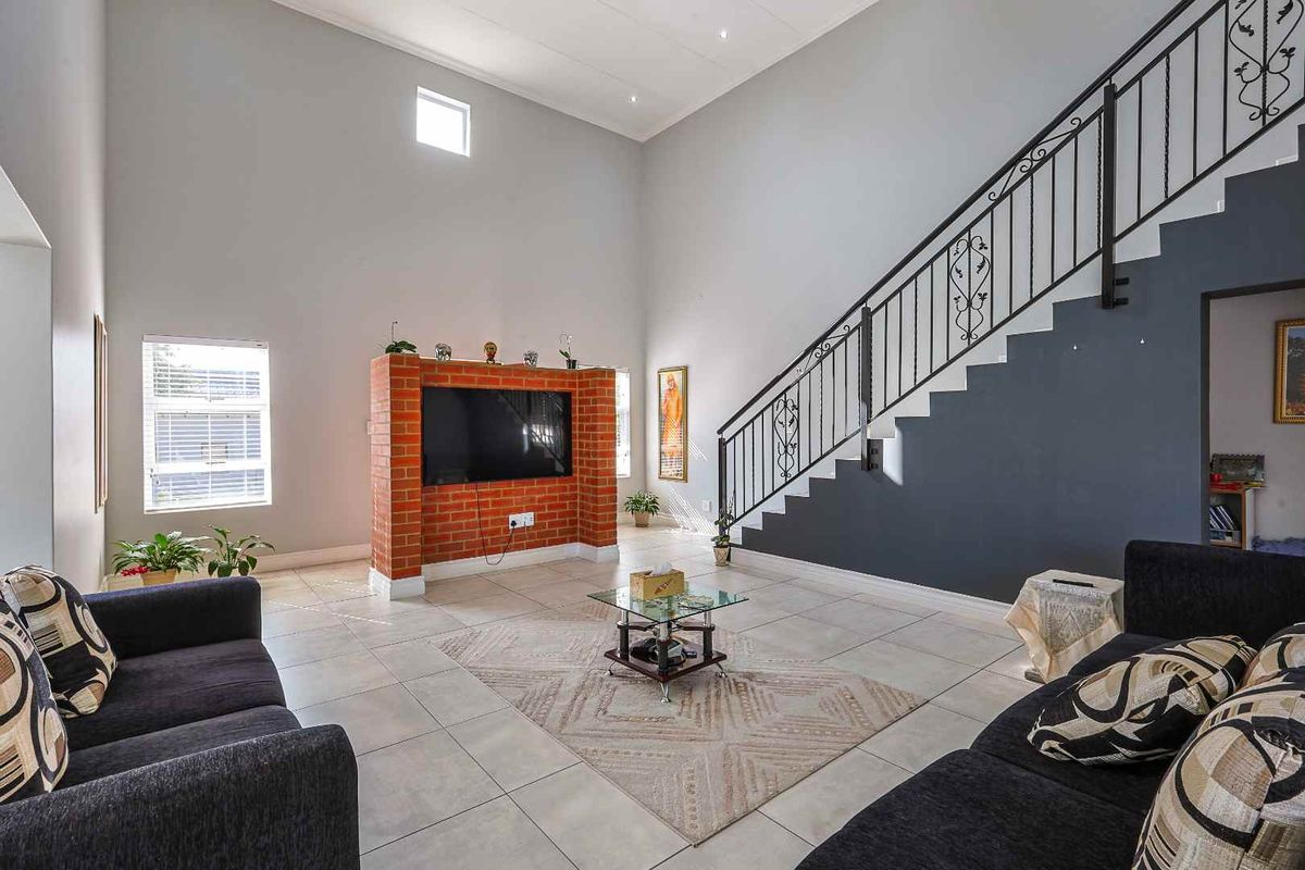 Spacious living room featuring high ceilings, tiled flooring, a central brick feature wall for media, and a staircase with decorative wrought iron railings.