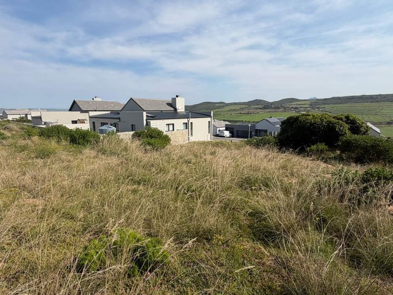 A view of the vacant residential land featuring natural grass coverage with surrounding modern residential properties and rolling hills in the background.