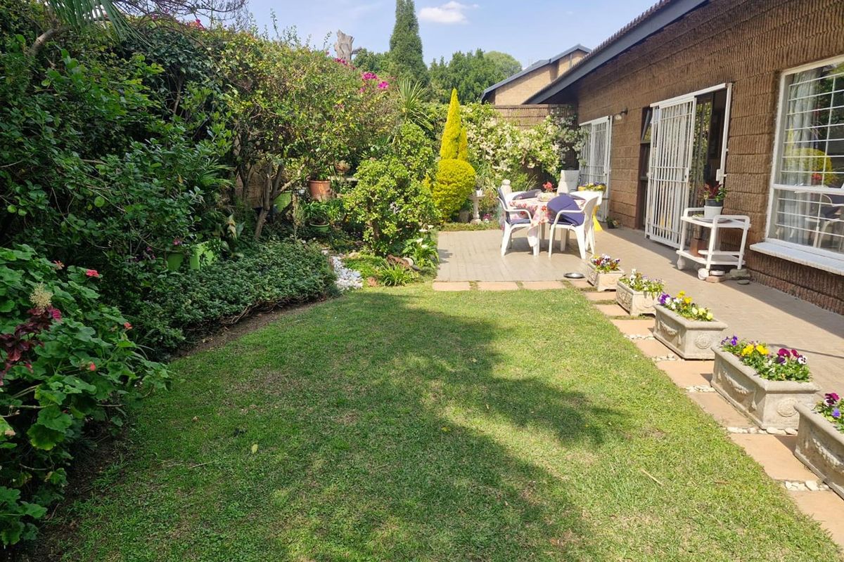 A well-maintained rear garden featuring a paved patio area, established landscaping, and direct access to the townhouse interior via security gates.