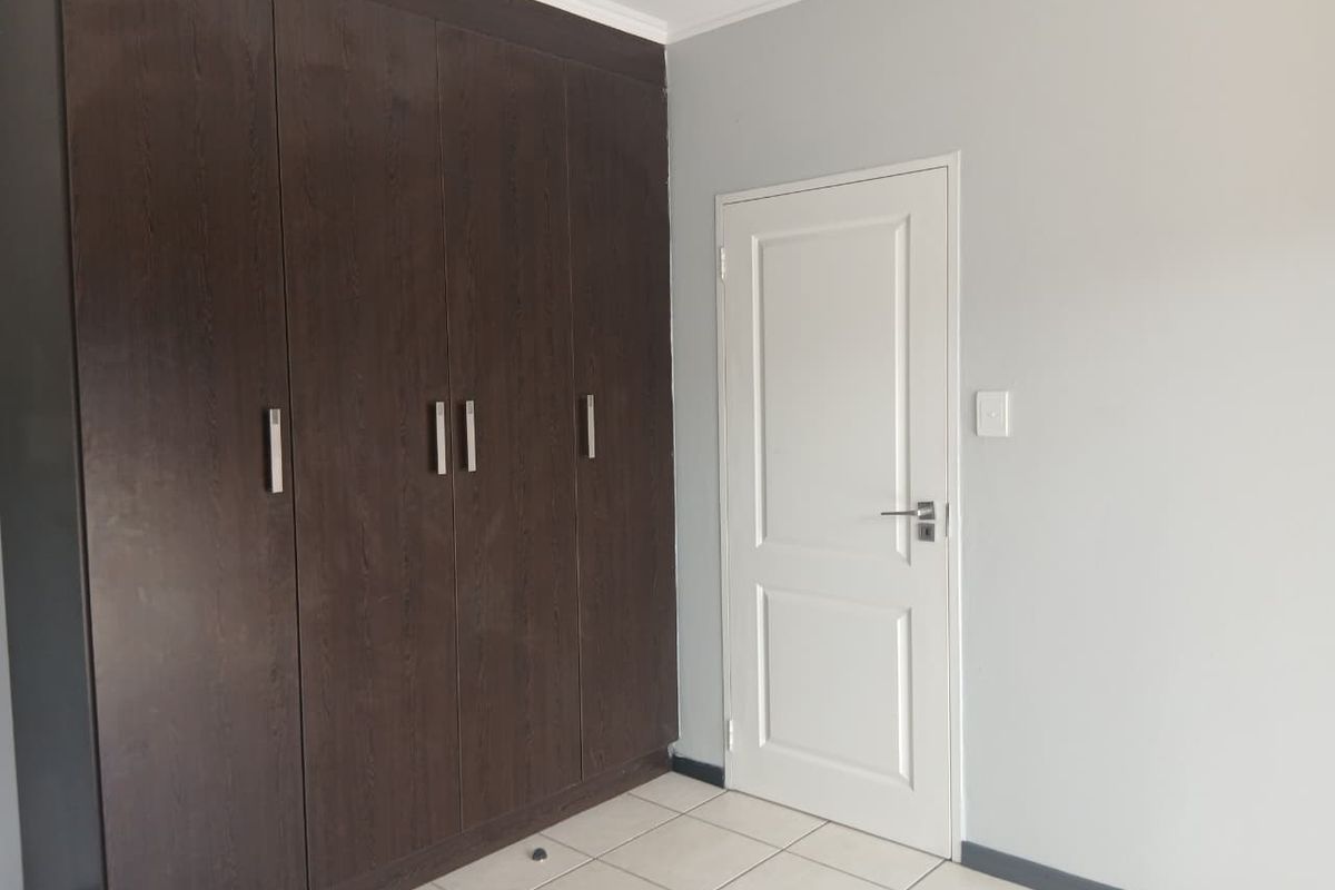 A bedroom featuring dark wood built-in cupboards, tiled flooring, and a white interior door.