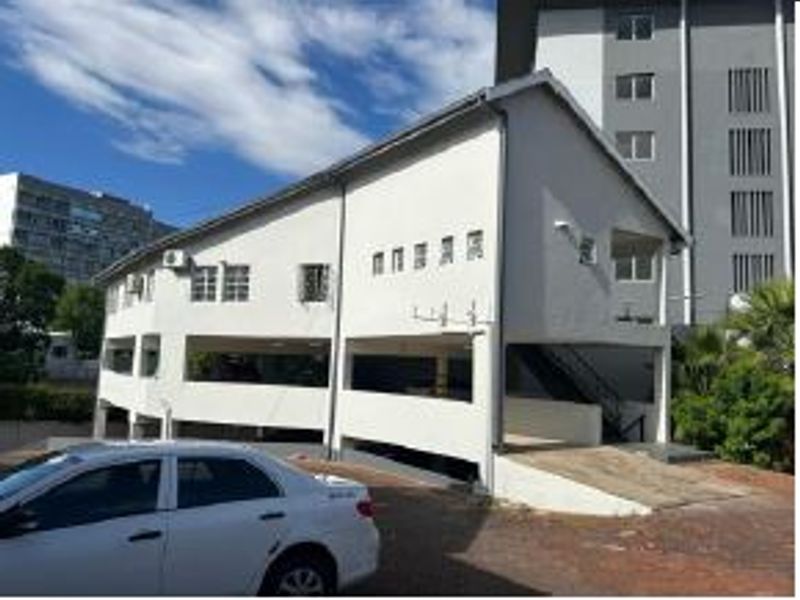 Exterior view of a multi-level office building featuring a pitched roof, security bars on windows, and an external staircase with paved driveway access.