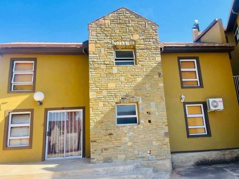 Rear elevation of a two-story house featuring stone cladding, a sliding glass door, and an external air conditioning unit.