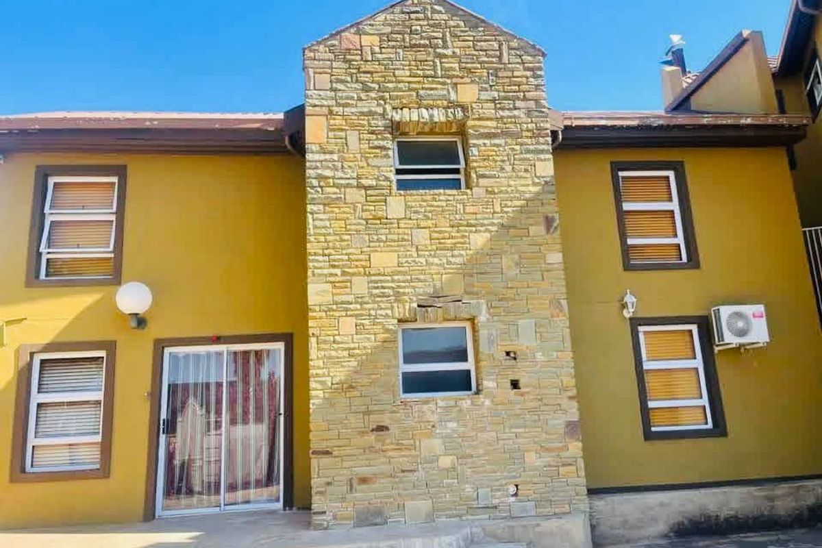 Rear elevation of a two-story house featuring stone cladding, a sliding glass door, and an external air conditioning unit.