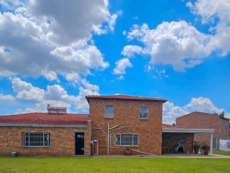 Rear view of a face-brick small holding property featuring a tiled roof, solar water heating system, and a covered patio area set in a garden.