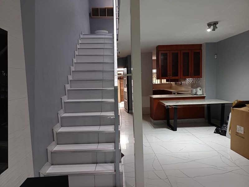 Open plan living area featuring a tiled staircase and a kitchen with wooden cabinetry and a breakfast bar island.