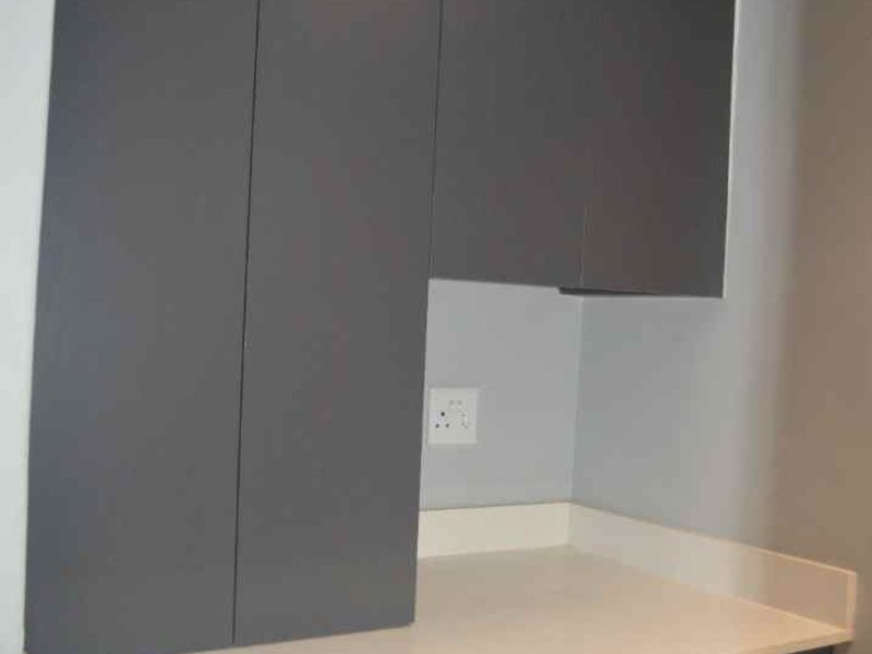 A modern kitchen area featuring sleek dark grey built-in cabinetry and a clean white stone countertop with an integrated electrical outlet.
