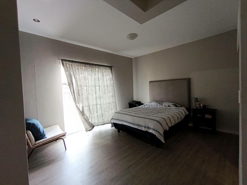 Spacious bedroom featuring laminate flooring, a recessed ceiling design, and a sliding door providing access to natural light.