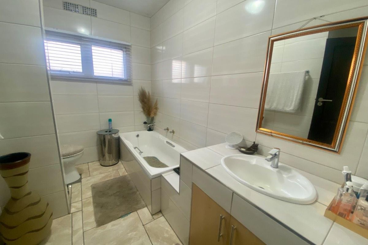 A functional bathroom featuring a built-in bathtub, a vanity with a basin, and full-height wall tiling.