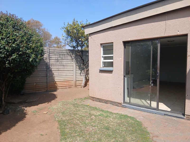 Rear view of the cottage featuring a sliding glass door, paved patio area, and a precast concrete boundary wall in the garden.