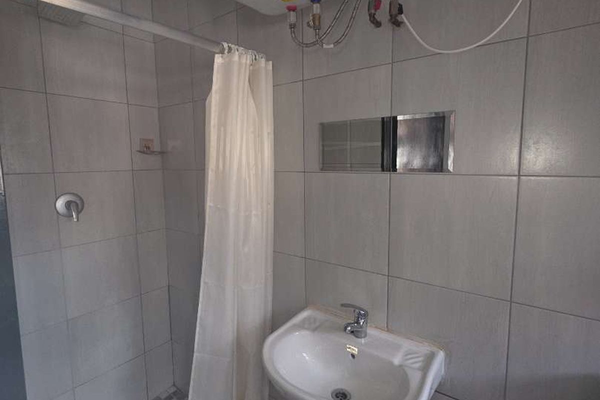 A functional bathroom featuring a pedestal basin, shower enclosure, and wall-mounted electric water heater with neutral tiled finishes.