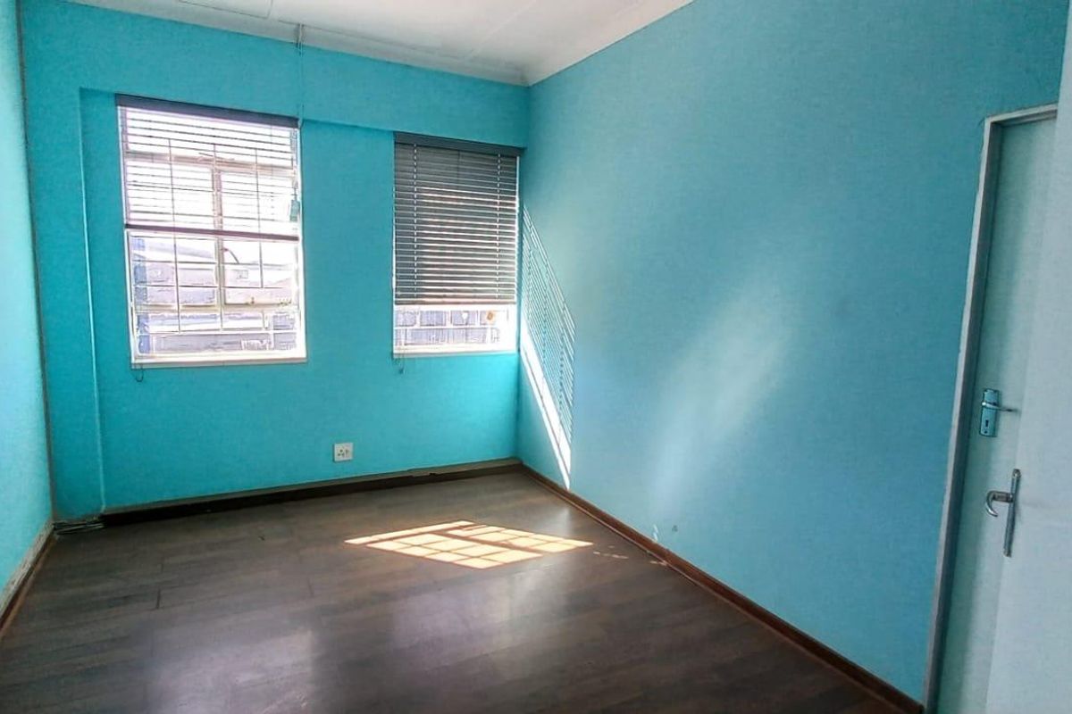 An empty bedroom featuring laminate flooring, bright blue walls, and two windows with fitted blinds.