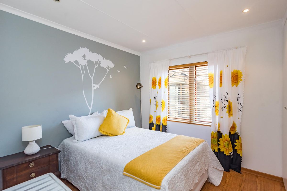 A well-maintained bedroom featuring laminate flooring, recessed downlights, and a feature wall with a decorative decal, offering a bright and comfortable living space.