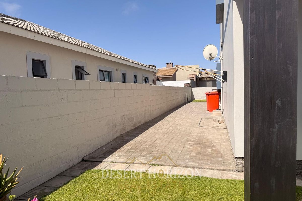 A side exterior area featuring a paved walkway, boundary wall, and wall-mounted clothesline, providing functional outdoor space along the side of the property.