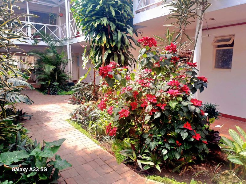 A landscaped courtyard area featuring brick paving and lush garden beds, situated between apartment building wings with balcony access.