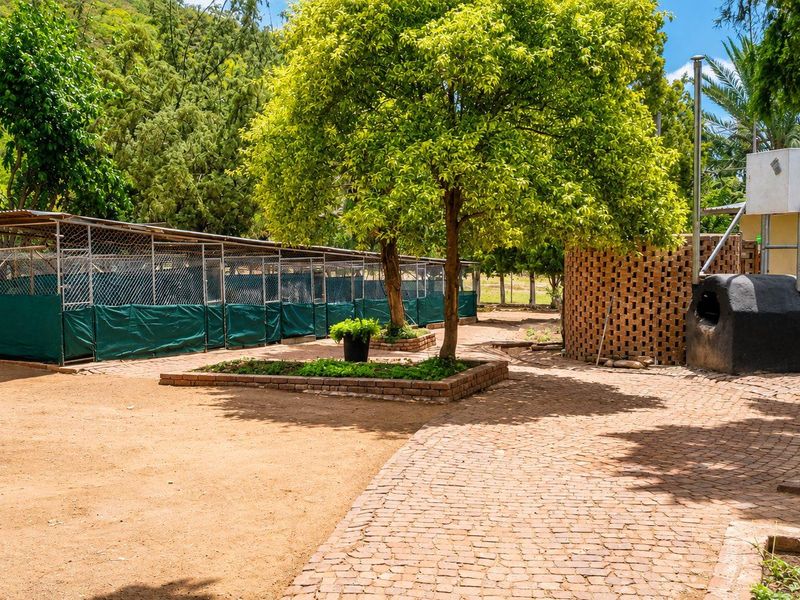 Outdoor area featuring brick paved pathways, established trees, brick planter beds, and a series of fenced enclosures suitable for small holding use.