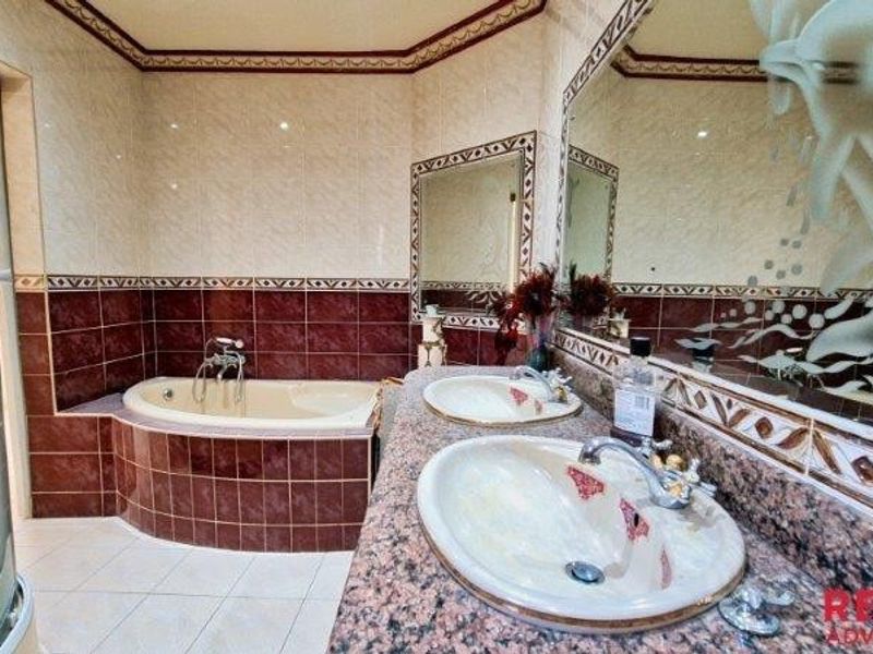 Spacious bathroom featuring a dual vanity with granite countertops, a tiled drop-in bathtub, and a separate shower enclosure with decorative wall mirrors.