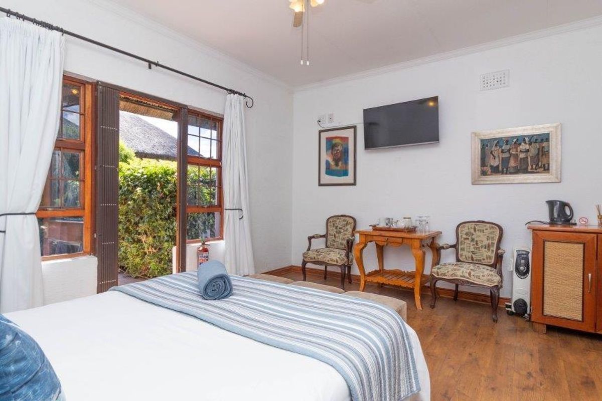 A comfortable bedroom featuring wood-look flooring, a ceiling fan, and direct access to an outdoor patio area through wooden-framed glass doors.