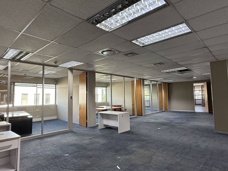 Open-plan office space featuring glass partitioned rooms, suspended ceilings with recessed lighting, and carpeted flooring throughout.